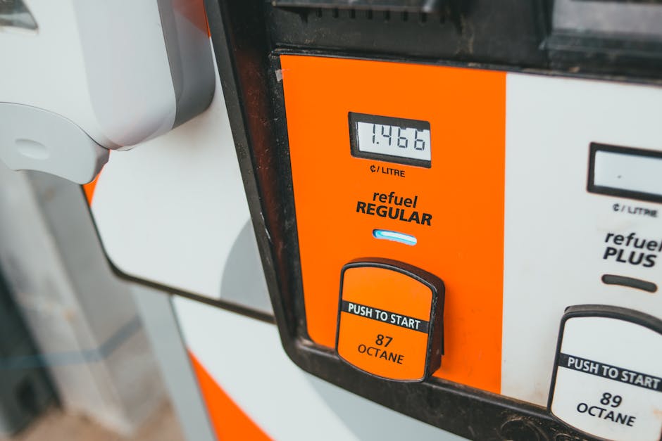 Close-up image of a fuel pump with an orange and white design, displaying a digital screen showing 1.4466 liters of fuel dispensed. The pump features a black button labeled 'PUSH TO START' and an orange octane rating indicator marked '87 OCTANE'. The surrounding environment suggests it is located at a fuel station, with part of a nozzle visible on the left side of the image. This scene illustrates the process of refueling, which is a typical part of home relocation logistics and furniture transport during a house move, supported by services such as Man with Van Finsbury Park specializing in removals and packing. The lighting appears natural, and the focus is on the fuel pump's operational interface, emphasizing the ease of fuelling vehicles used for moving items between locations.